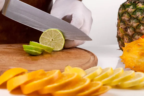 Chef rebanando lima en una tabla de cortar de madera entre frutas — Foto de Stock