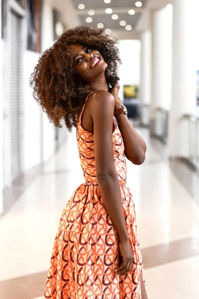 Кудрявая афро-американка в длинном платье улыбается в камеру . — стоковое фото