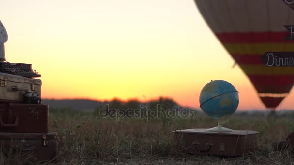 Balon na ogrzane powietrze leci się na podłoże i globe model z stare walizki na pierwszym planie. Koncepcja podróży — Wideo stockowe