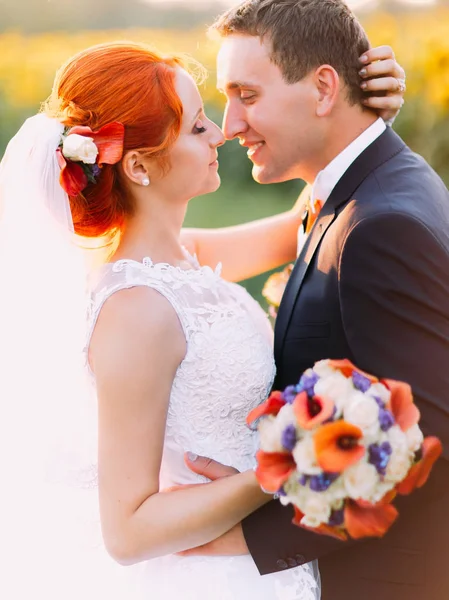 Портрет яскравої щасливої рудої нареченої і красивого нареченого люблять дивитися один на одного на сонячному полі соняшнику — стокове фото