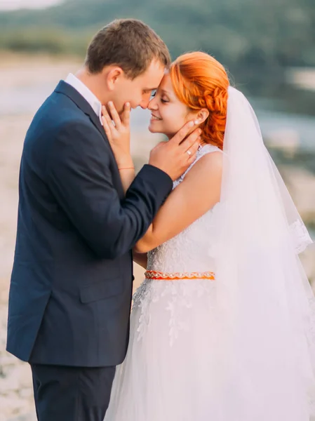 Atractiva pareja joven boda amorosamente se miran entre sí. Orilla con piedras en el fondo — Foto de Stock