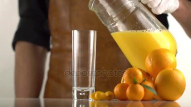 Adam portakal ve mandalina yakınında bulunan boş cam içine portakal suyu yağıyor.
