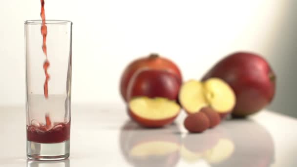 Die Nahaufnahme, wie das leere Glas mit dem roten Saft vor dem verschwommenen Hintergrund der Äpfel voll wird. — Stockvideo