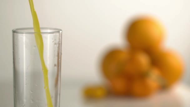 The empty high glass is becoming full with the orange juice at the blurred background of the oranges and mandarins. Close-up. — Stock Video