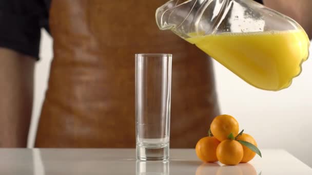 De hoge snelheid van de man die het SAP van de karaf gieten in het hoge glas geplaatst in de buurt van ther mandarijnen. — Stockvideo