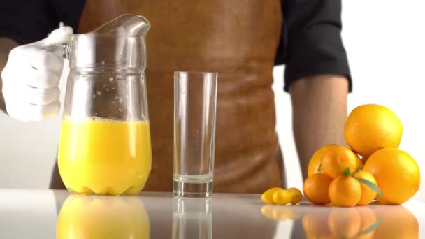 De hoge snelheid van de kookplaat gieten het oranged SAP met de karaf in het hoge glas ligt in de buurt van de mandarijnen. — Stockvideo