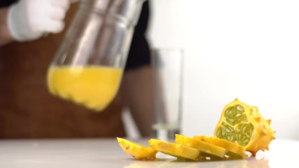 The close-up composition of the cut into slices kiwano at the blurred background of the cooker pouring the orange juice into the high glass.