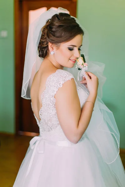 Coy sposa in abito bianco in posa, tenendo carino piccolo boutenniere e guardando oltre la spalla — Foto Stock