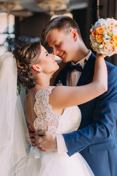 Amada pareja de boda. Hermosa novia con ramo y novio guapo de pie en el interior, ventana agaísta. Esposo besándose abrazando a su esposa — Foto de Stock