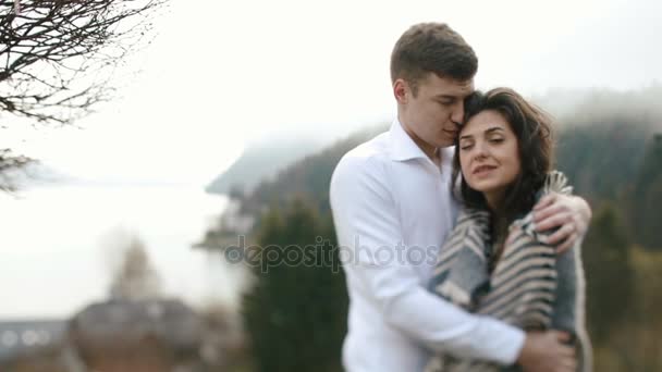 A composição sensível do casal abraçando no fundo da floresta e montanhas. A menina está embrulhada na xadrez . — Vídeo de Stock