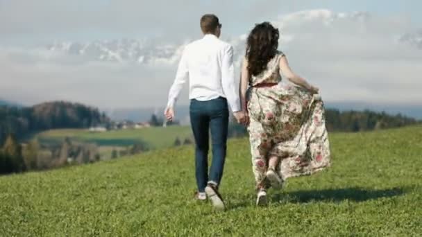 La vue arrière du couple joyeux qui court dans la prairie des montagnes . — Video