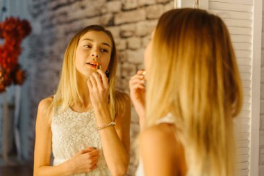 Sarışın genç dudaklar uyguluyor. Aynaya yakın çekim yansıma.