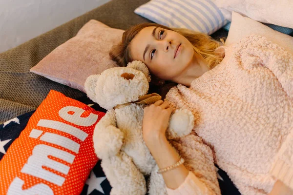 Die Seitenansicht des träumenden Teenie-Mädchens, das mit dem Teddybär auf den Kissen liegt. — Stockfoto