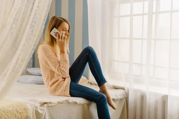 아름 다운 젊은 여자는 침실에서 휴대 전화 통화 하는 동안 침대에 앉아. — 스톡 사진