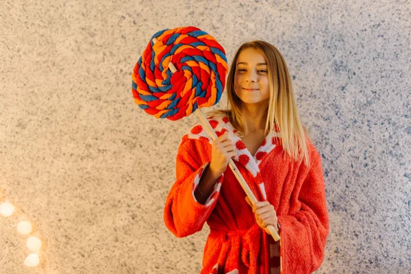 De lachende tiener in de mantel houdt het enorme lollipop kussen. — Stockfoto