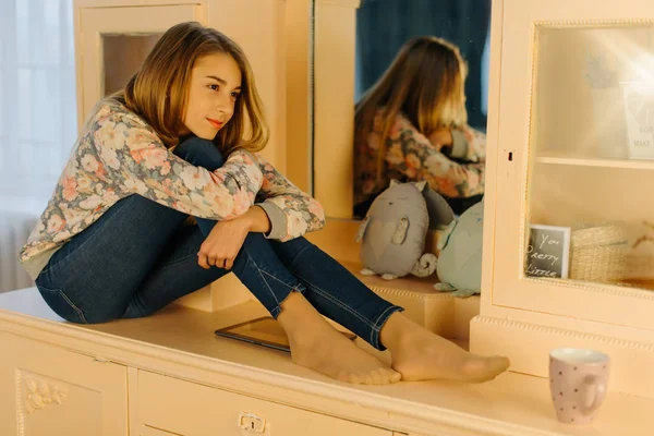 The close-up view of the smiling teenage girl hugging the knees and sitting on the dresser. — Stock Photo, Image