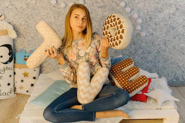 The throughtful teenager is holding the cushions with love letters and sitting on the sofa. — Stock Photo, Image
