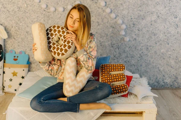 The cushions with love letters are held by the young teenager while sitting on the sofa. — Stock Photo, Image