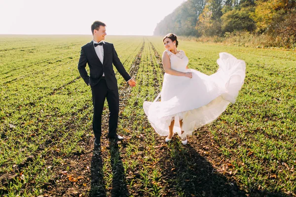 Härlig utsikt över nygifta i det gröna fältet. Brud leker med sin brudklänning. — Stockfoto
