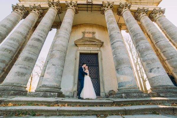 A vőlegény a menyasszonyt megcsókolta a fejen állva, közel a régi épület. — Stock Fotó