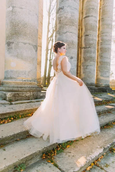 La vista laterale della sposa nel lungo abito pomposo in piedi sulle scale dell'antico edificio . — Foto Stock