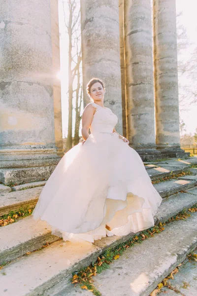Усміхнена наречена крутиться в помпезній весільній сукні, що стоїть на сходах старовинної будівлі . — стокове фото
