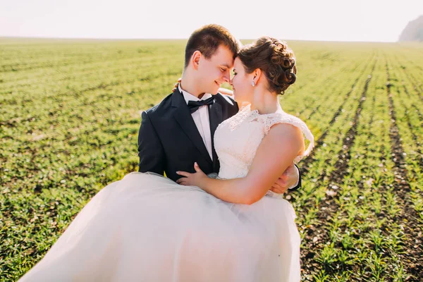 Romántico retrato de cerca del novio llevando a la novia en el fondo del campo verde . —  Fotos de Stock