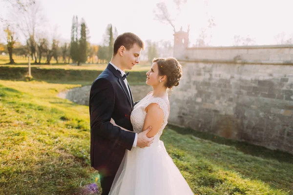 The horizontal side portrait of the smiling newlywed couple hugging near the mansion in the spring. — Stock Photo, Image