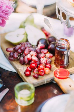Meyve kompozisyonu. Orada Erik, yeşil armut, kara üzüm ve sulu kiraz kavanoz ve küçük mum bar yer ahşap tahta üzerinde yalan.