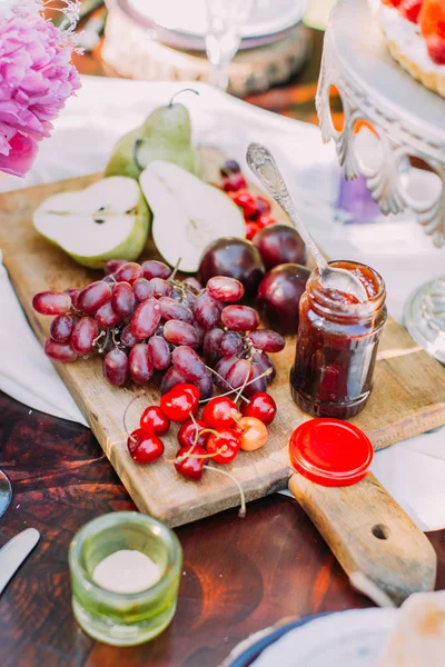 Sulu kırmızı üzüm, kiraz, yeşil armut, Erik ve düğün pastası yakınındaki ahşap tahta üzerinde bulunan kavanoz çubuğu yan portresi.