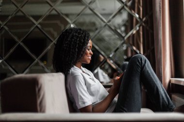 Kanepede oturan ve bir telefon tutarak mutlu siyah kadın. Bir haberci yazarak kadın.