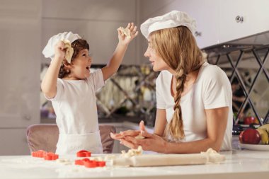 Mutlu anne ve oğlu ile hamur oynuyor. Beyaz önlük ve şapka giyen aile.