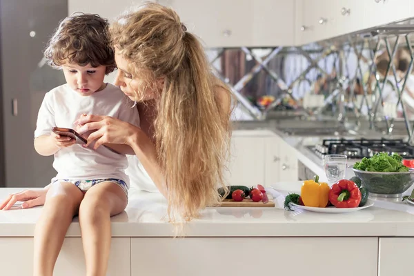 Anne ve küçük oğlu telefon ekranına bakarak. Mutfak konumu. — Stok fotoğraf