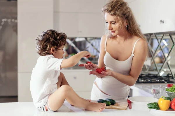 Mutlu genç anne ile küçük oğlu mutfakta. Anne ve oğlu beyaz elbise giyen. — Stok fotoğraf