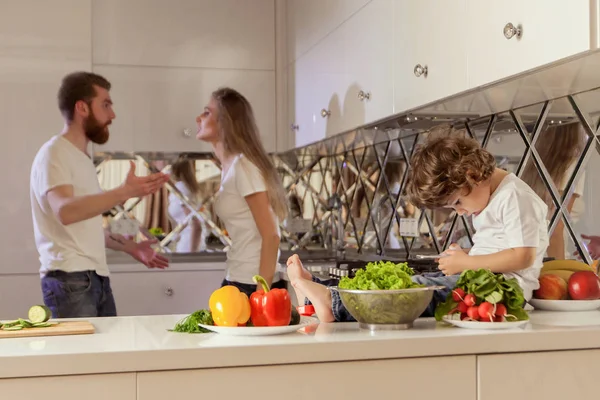 Traurig dreinblickender Junge mit ihren kämpfenden Eltern im Rücken. Junge schaut auf den Handybildschirm. — Stockfoto