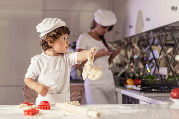 Baking concept. Mother and son baking in the kitchen wearing white aprons and hats. — Stock Photo, Image