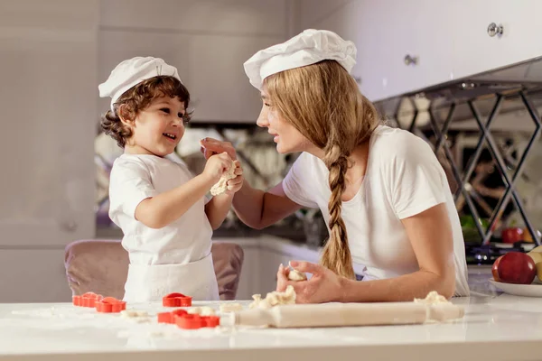 Photo of happy mother and her son wearing white aprons and hats making a dough. — Stock Photo, Image