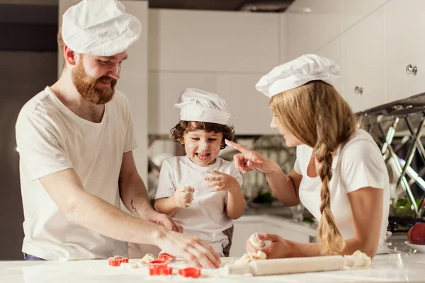 Happy parents together with their little son making a dough for baking cookies. — Stock Photo, Image