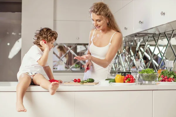 Anne yemek küçük oğlu ile birlikte modern beyaz mutfakta yaptırıyor. — Stok fotoğraf