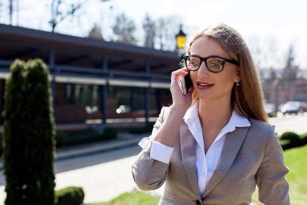 Succesvolle jonge zakenvrouw praten over de telefoon outsibe. Aantrekkelijke blondine met lang haar. — Stockfoto