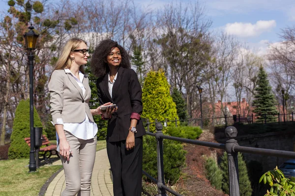 Одна чёрная и одна белая деловая женщина, гуляющая по парку и разговаривающая . — стоковое фото
