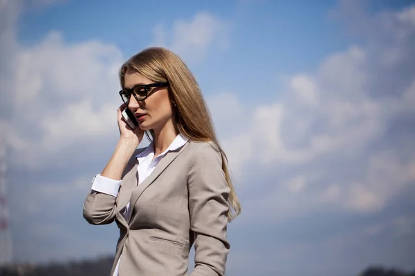 Jonge aantrekkelijke zakenvrouw in pak praten aan de telefoon. Hemelachtergrond. — Stockfoto