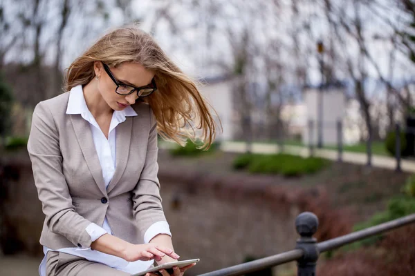 Empresária com longos cabelos loiros sentada no parque com o tablet em suas mãos — Fotografia de Stock