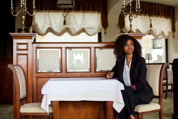 Mladé krásné černé podnikatelka sedí u stolu s tabletem v ruce. Žena nosí oblek. — Stock fotografie