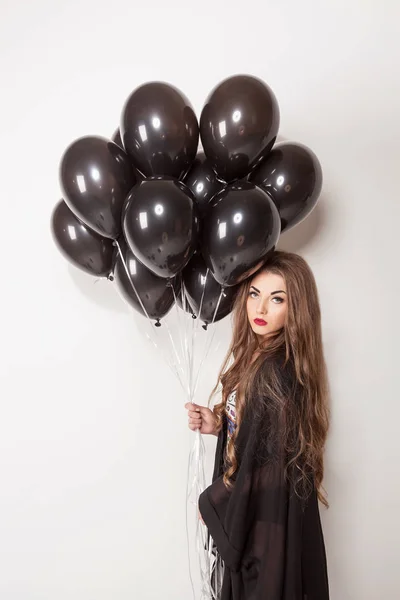 Mooie jonge vrouw poseren voor de camera op een witte achtergrond met zwarte baloons. — Stockfoto