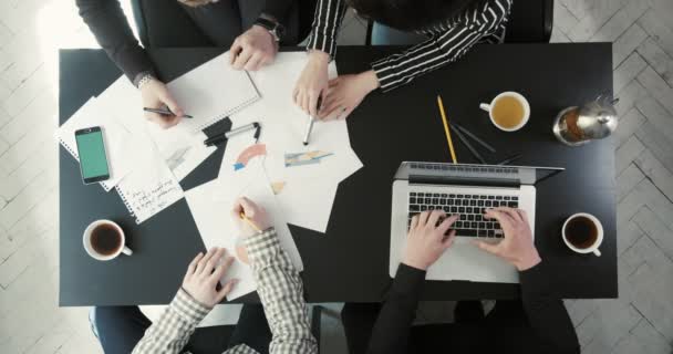 Вид зверху руки чотирьох людей, що тримають бізнес-плани і графіку, друкують на ноутбуці і п'ють чай. Композиція бізнесу . — стокове відео