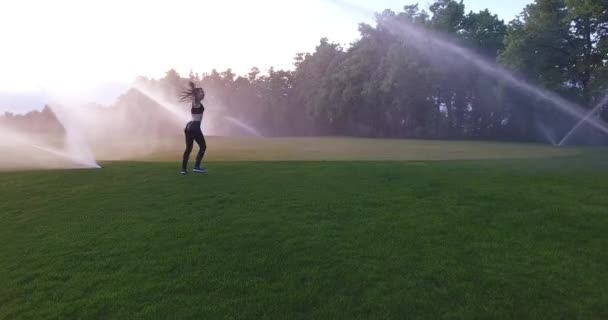 The slender woman is dancing, spinning and running among the sprinklers. — Stock Video
