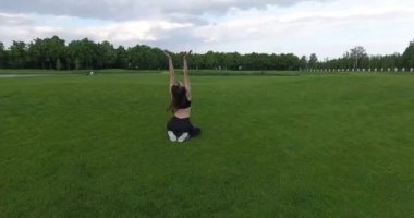 Kadınla çimenlerin üzerinde otururken pilates ve joga yapıyor. Yuvarlak görünümü.