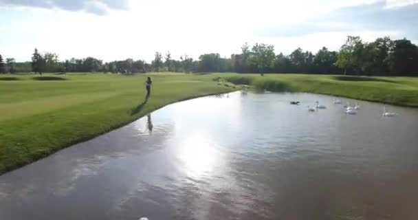 De achterkant van de jogging vrouw langs het gazon in de buurt van de rivier. De volledige snelheid. — Stockvideo