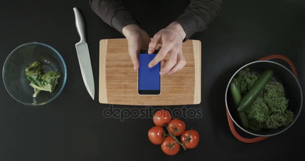 Haands rolando a tela do telefone. Mesa de cozinha com comida, faca e tábua de corte. Vista superior . — Vídeo de Stock